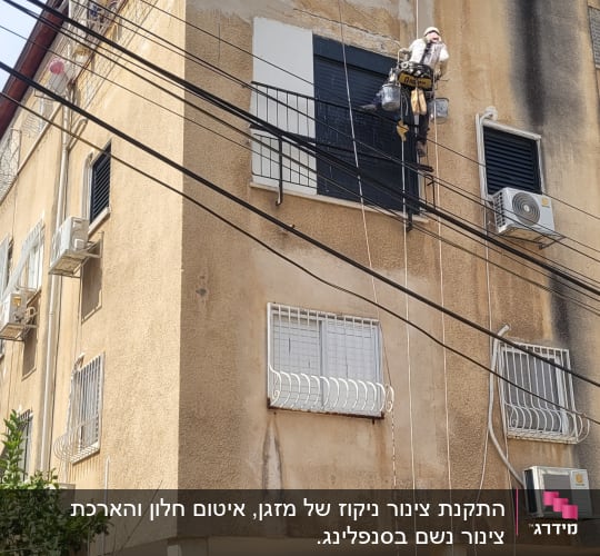 אדם עובד בגובה על קיר בניין עם ציוד בטיחות